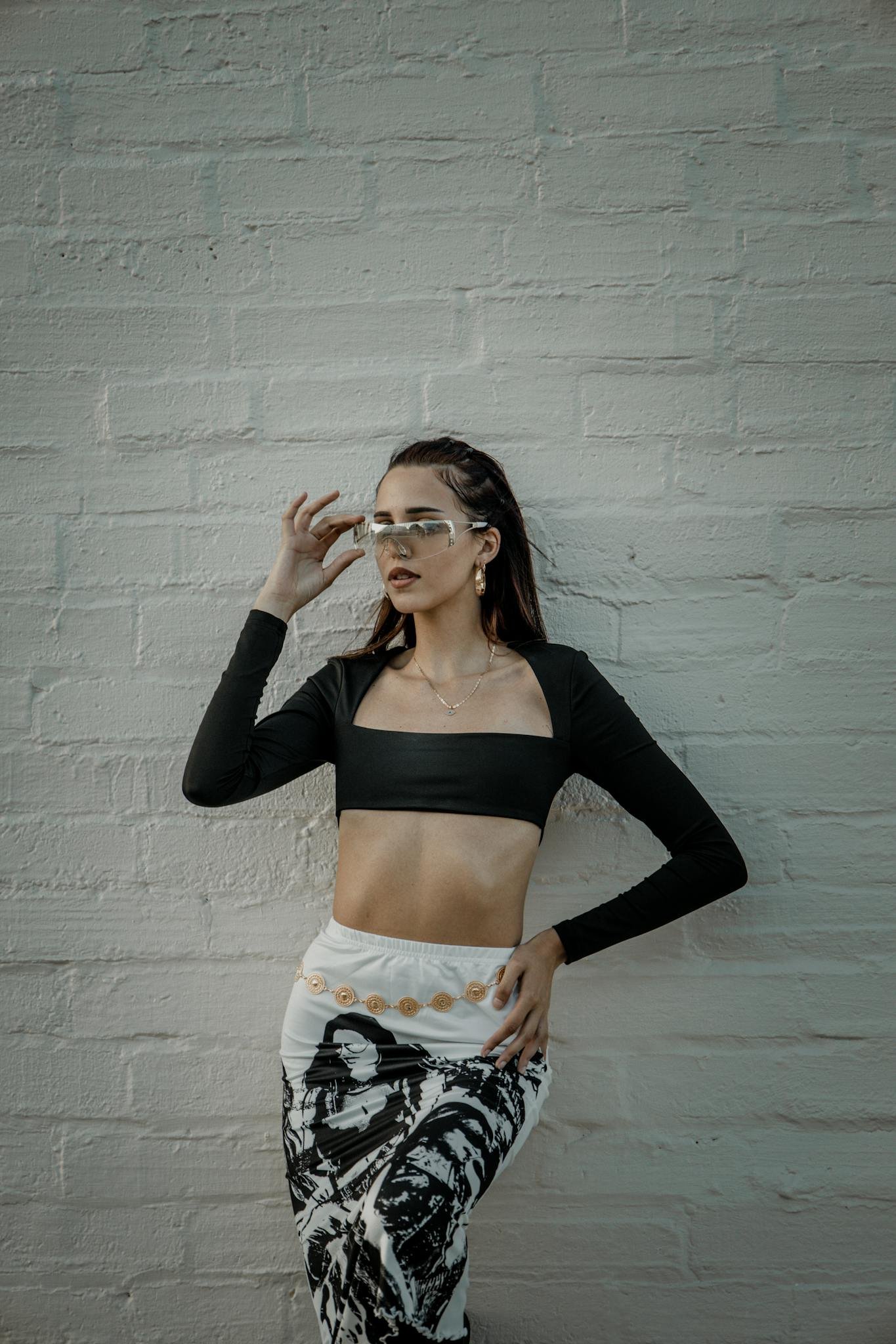 Fashionable woman in stylish attire posing against a brick wall, showcasing modern style and confidence.