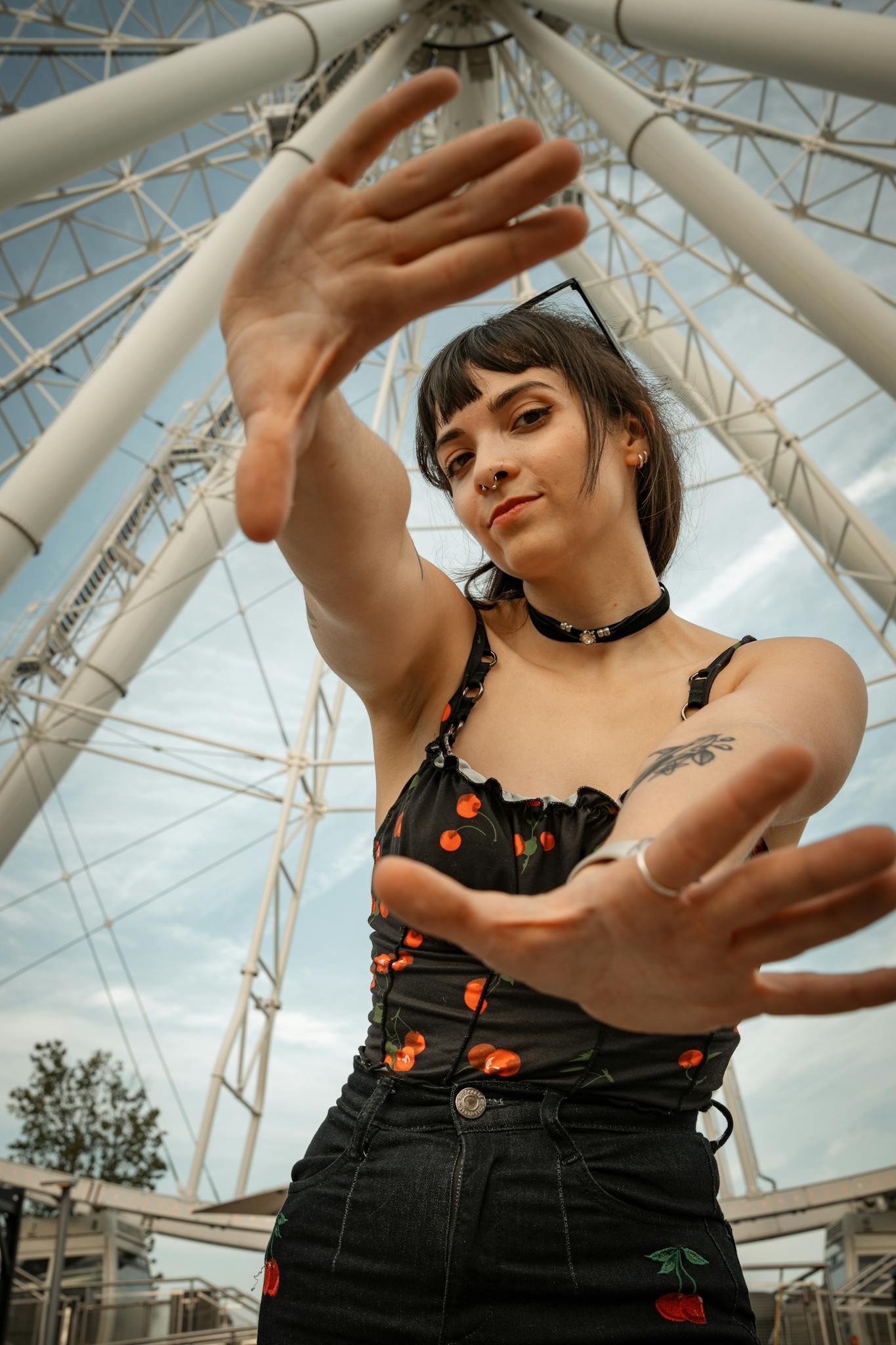 Young woman posing confidently with a ferris wheel background, showcasing modern fashion.